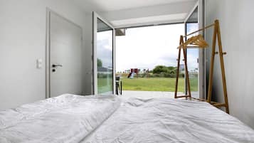 Una camera da letto con un letto, un appendiabiti in legno e una porta-finestra in vetro scorrevole che dà su uno spazio esterno con un'area giochi.