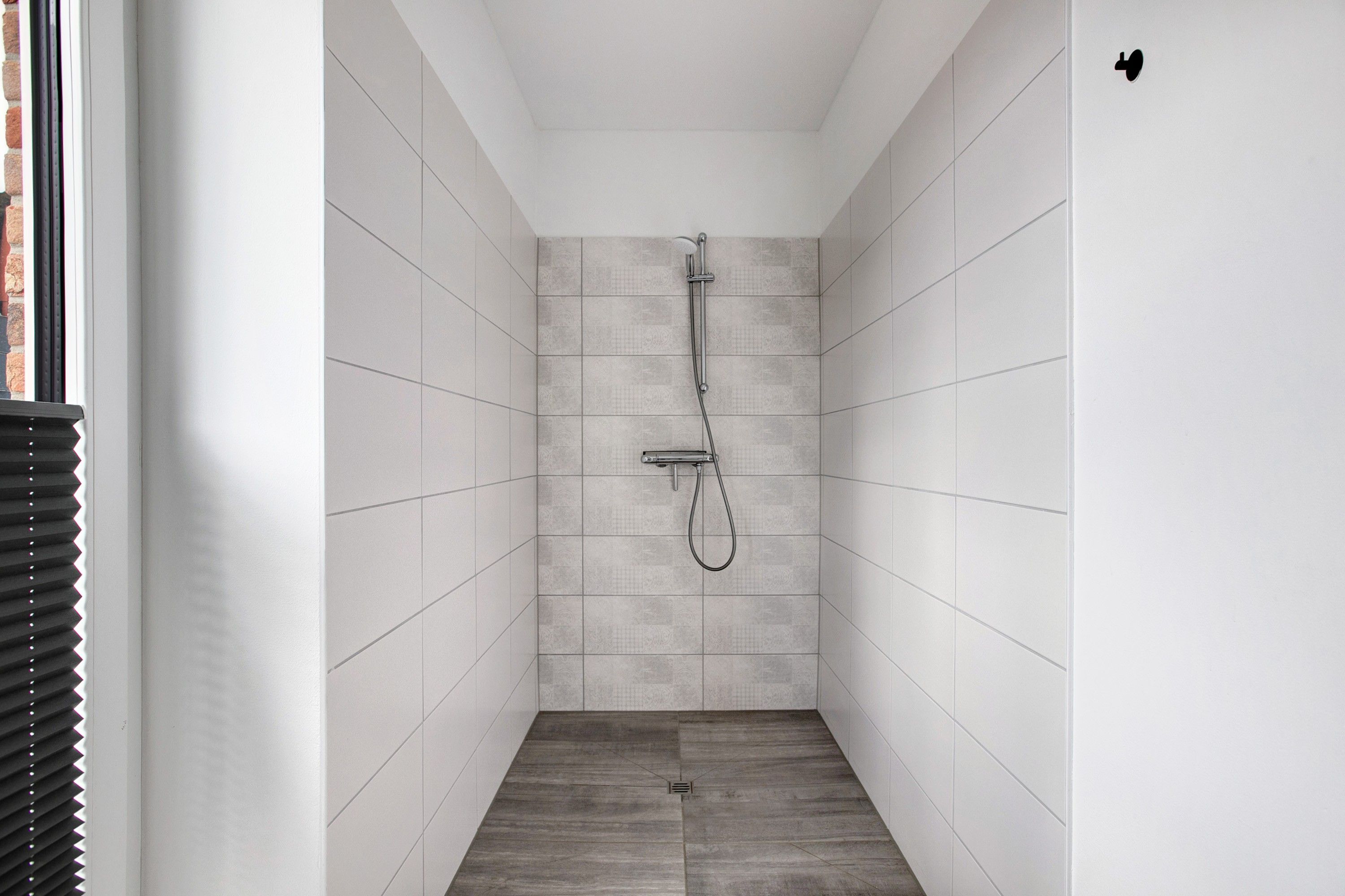 A narrow, tiled shower room with a shower head and hose.