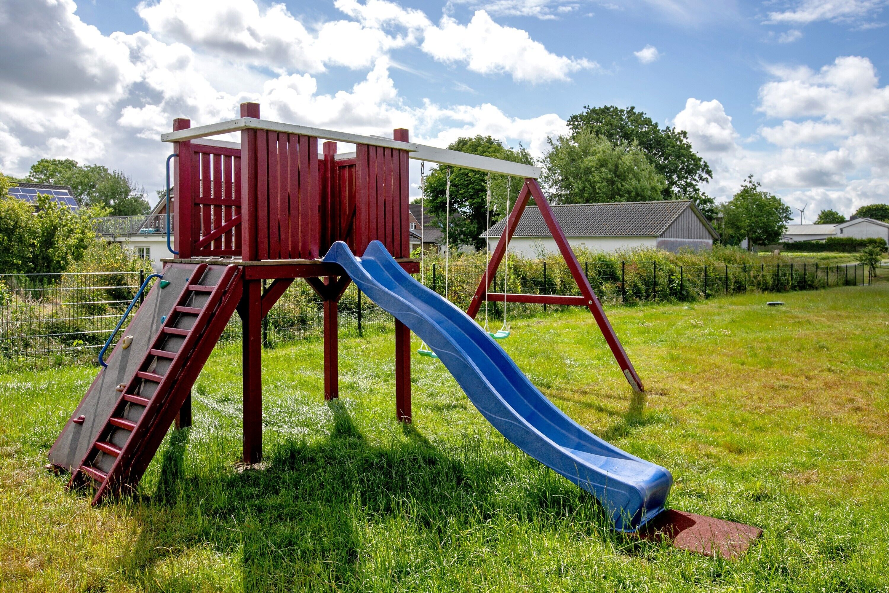 Un parque infantil con una casita roja, un tobogán azul y columpios.