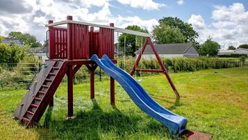 Un parque infantil con una casita roja, un tobogán azul y columpios.