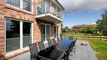 Ein zweistöckiges Backsteinhaus mit Balkon, einer Terrasse mit Tisch und Stühlen mit Glastischplatte und ein kleines rotes Spielzeugauto.