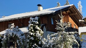 Puinen mökki, jossa on kalteva katto, ja sen ympärillä on lumipeitteisiä puita.