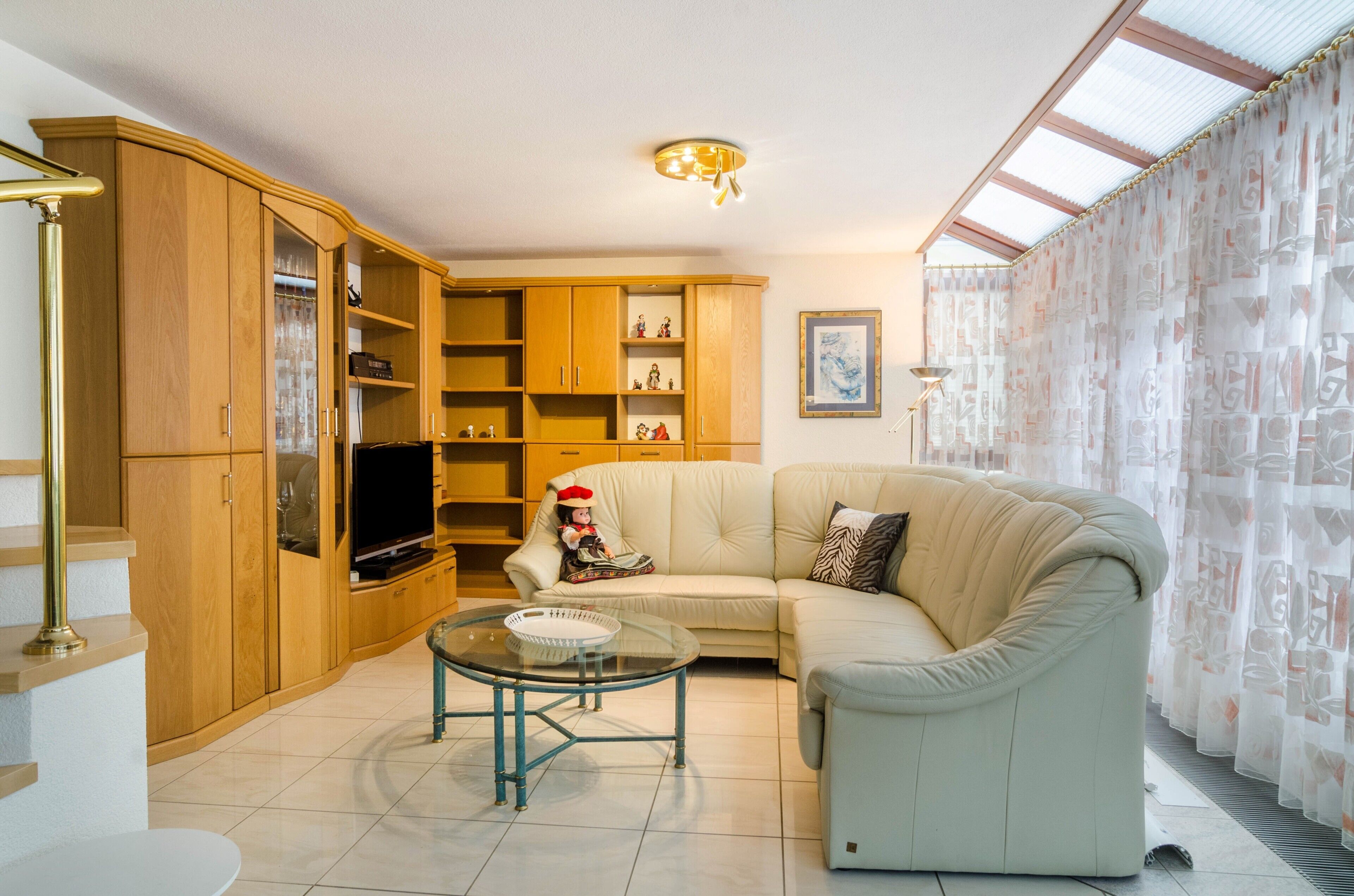 A living room with a sofa, a glass coffee table, wooden cabinets, a television, and a ceiling light fixture.