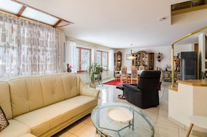 Un salon comprenant un canapé, un fauteuil noir, une table basse en verre et un meuble en bois.