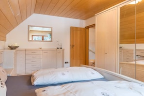 Une chambre avec un plafond en pente, un lit avec une literie blanche, une armoire en bois et un miroir au-dessus du lit.