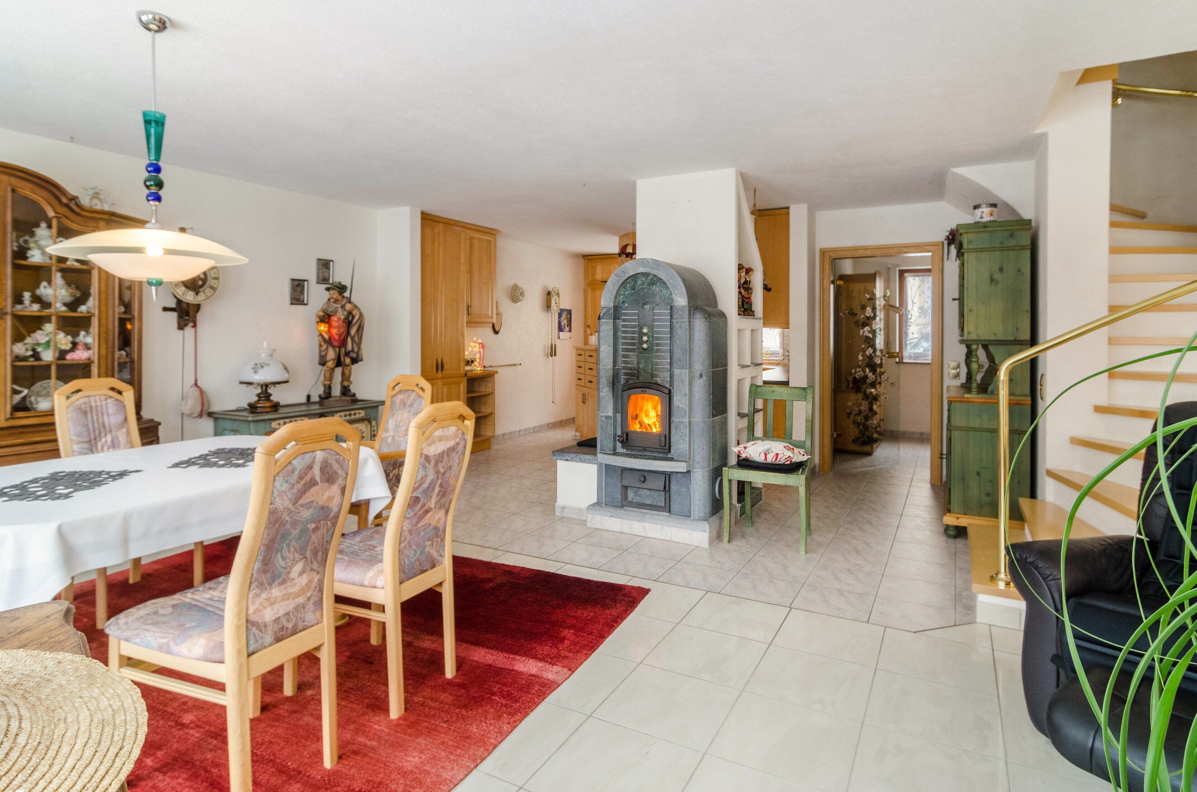 Un comedor con una mesa, sillas y un tapete rojo. Hay una chimenea con fuego visible.