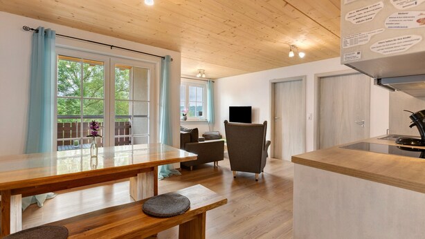 A modern kitchen with wooden countertops, a dining area with a bench, a TV, and a view of greenery outside. - Apartment 'Ferienwohnung Gauchach' with Shared Garden, Balcony and Wi-Fi (Löffingen)