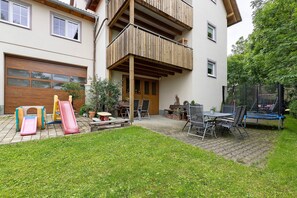 A residential building with a wooden balcony, a garage, a children's play area with slides, and a trampoline. - Apartment 'Ferienwohnung Gauchach' with Shared Garden, Balcony and Wi-Fi (Löffingen)