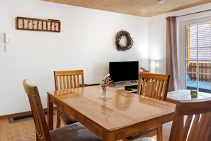 A dining area with a wooden table, chairs, a TV, and a window with a view. - Apartment 'Ferienwohnung Gutach' with Shared Garden, Balcony and Wi-Fi (Löffingen)