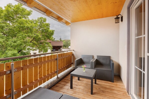 A balcony with a wooden floor, two wicker chairs, a small table with a vase, and a railing. - Apartment 'Ferienwohnung Gutach' with Shared Garden, Balcony and Wi-Fi (Löffingen)