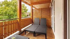 Una terraza de madera con barandilla, dos sillas grises con cojines y una mesita.