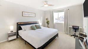 A bedroom with a bed, a nightstand, a ceiling fan, a window with curtains, and a desk with a chair.