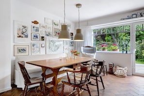 A dining area with a wooden table and chairs, pendant lights, and framed artwork on the wall.