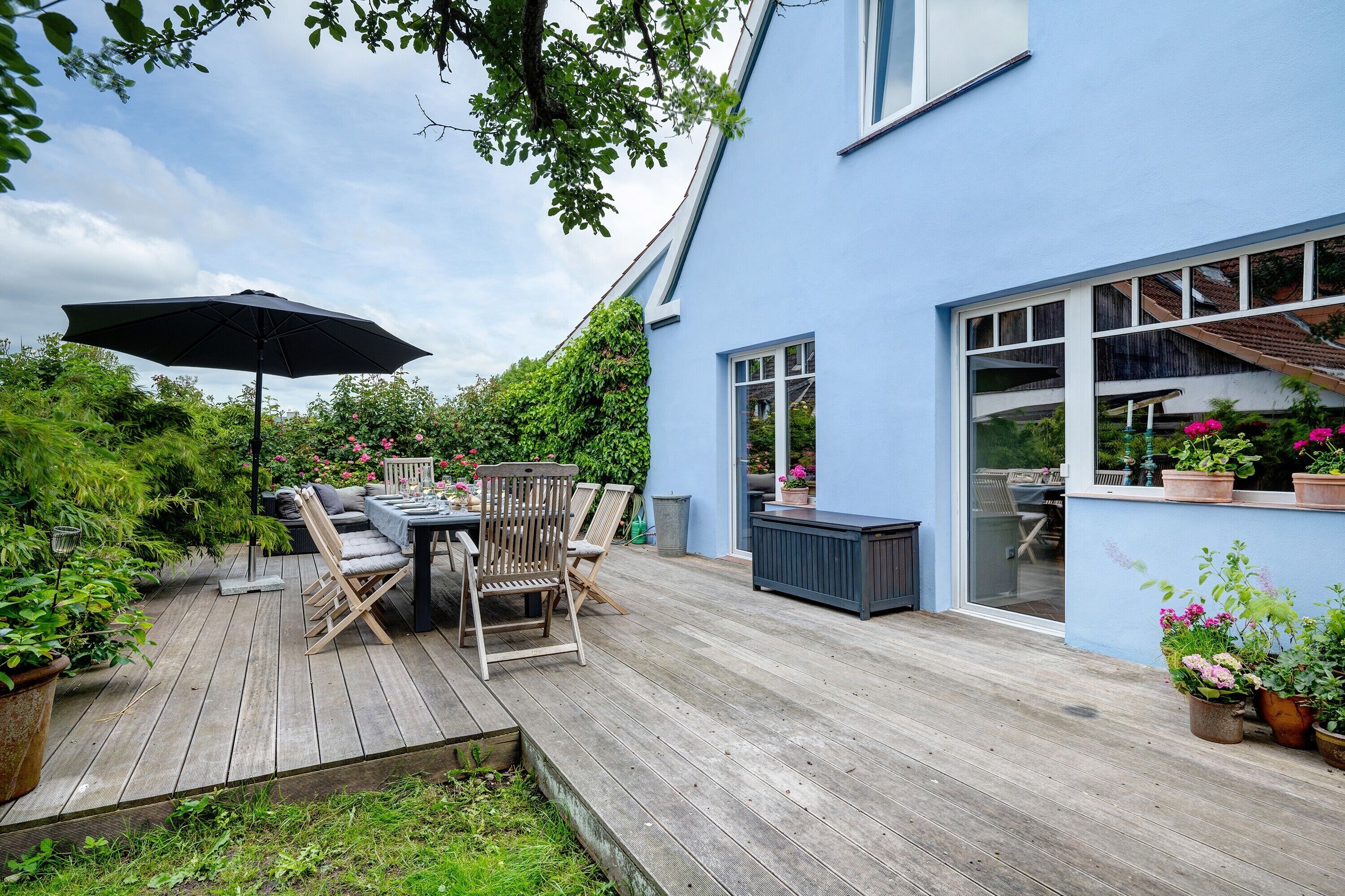 A blue house with a wooden deck, outdoor furniture, and potted plants.