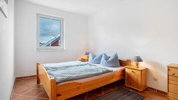 A bedroom with a wooden bed, a nightstand, a dresser, a window with a view, and a tiled floor.