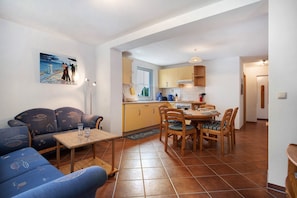A compact living space with a sofa, dining table, chairs, a kitchen area, and a painting on the wall.
