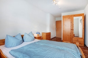 A bedroom with a bed, pillows, a nightstand, a lamp, a wooden wardrobe, and a door.