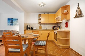 Une cuisine de taille réduite, dotée de meubles en bois, d’une table à manger avec des chaises et d’un sol carrelé.