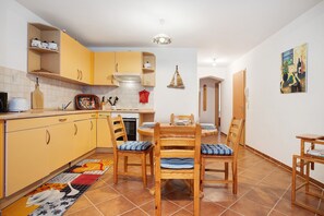Une cuisine avec des meubles de couleur jaune, une table à manger avec des chaises et un sol carrelé.