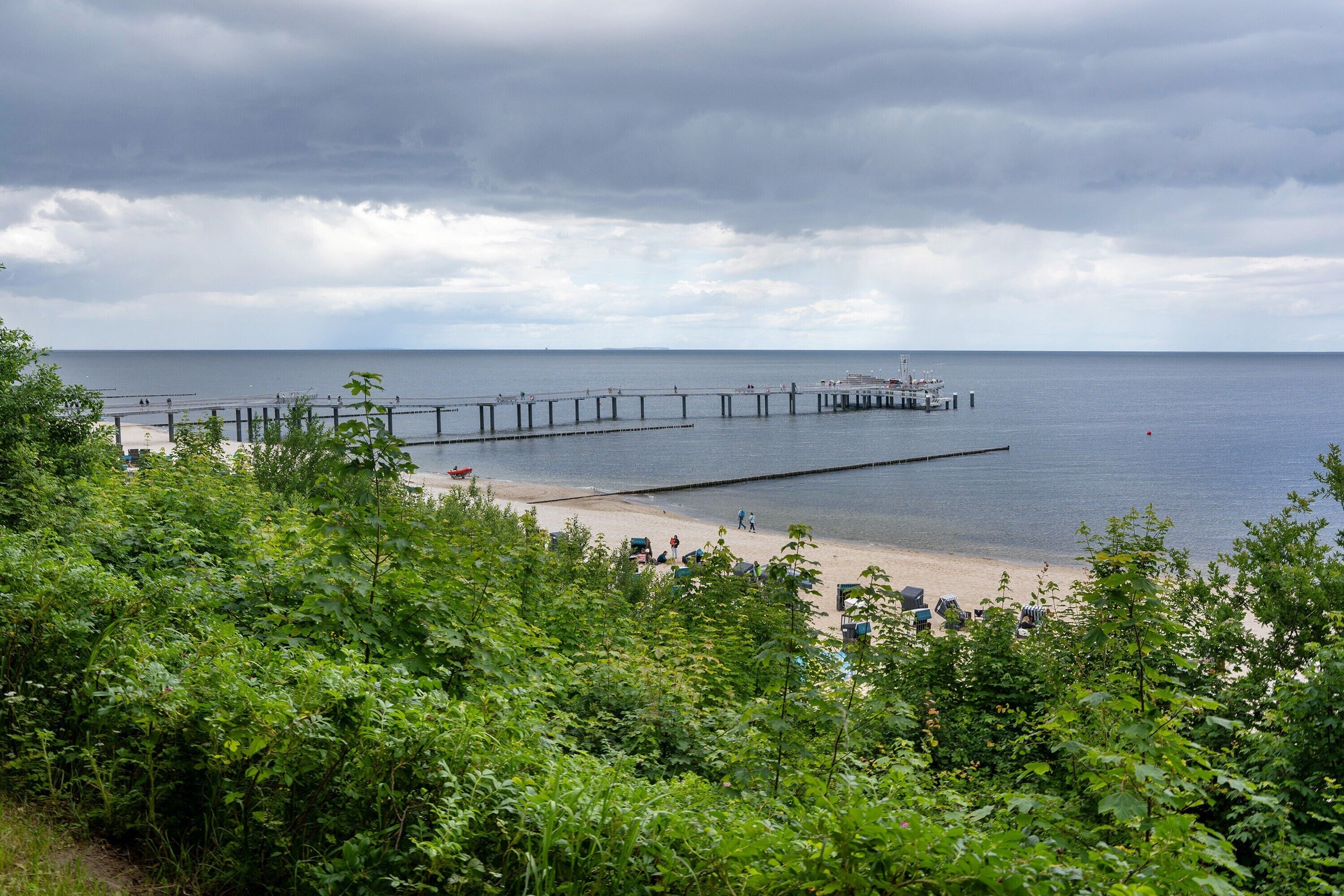 Een kustgezicht met een pier die in zee steekt, omringd door groen.