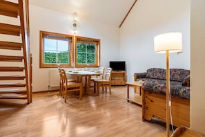 Une pièce comprenant une table à manger en bois, des chaises, un canapé, un téléviseur et une lampe.