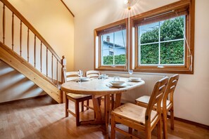 Un'area pranzo con tavolo e sedie in legno, una scala e una finestra vista verde.