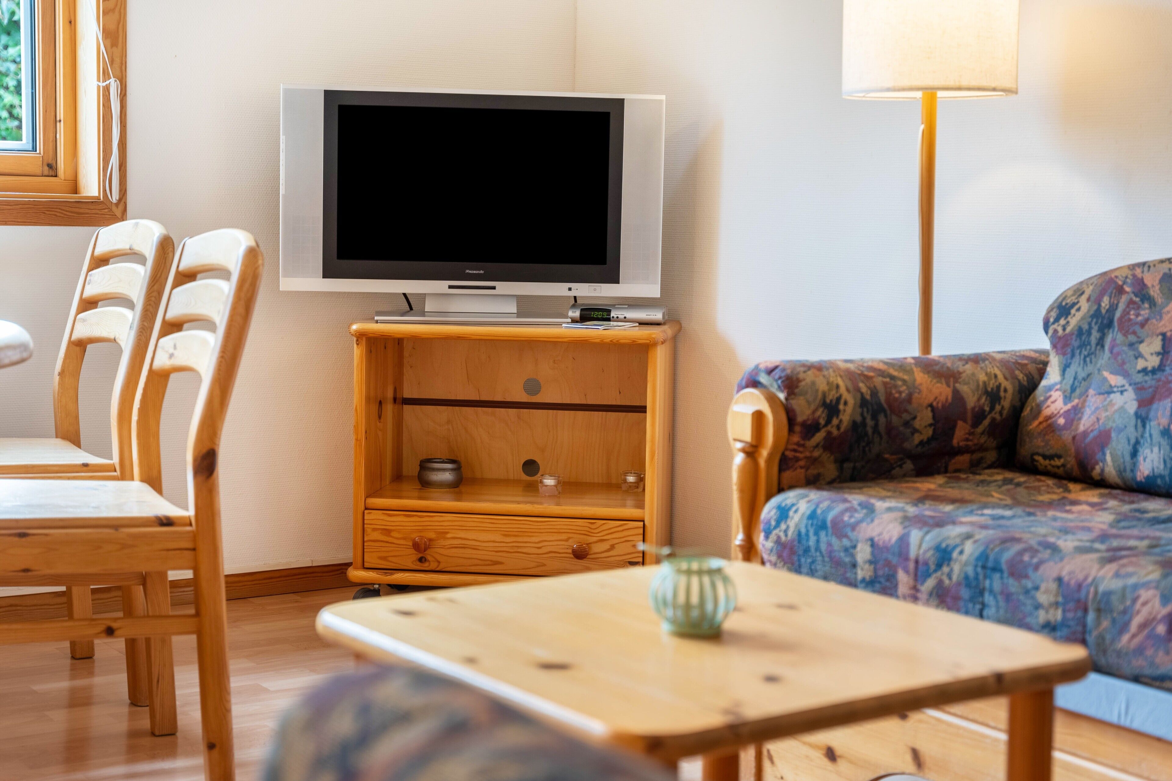 Ein Wohnzimmer mit Fernseher, Holzmöbeln, einer Couch und einer Lampe.