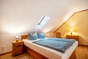 Una camera da letto con soffitto spiovente, una finestra a lucernario, un letto con biancheria azzurra, due comodini con lampade e un comodino in legno.