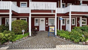A two-story building with a red facade, white balconies, and a cobblestone entrance.