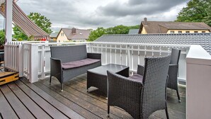 A covered outdoor seating area with wicker furniture and a white railing.