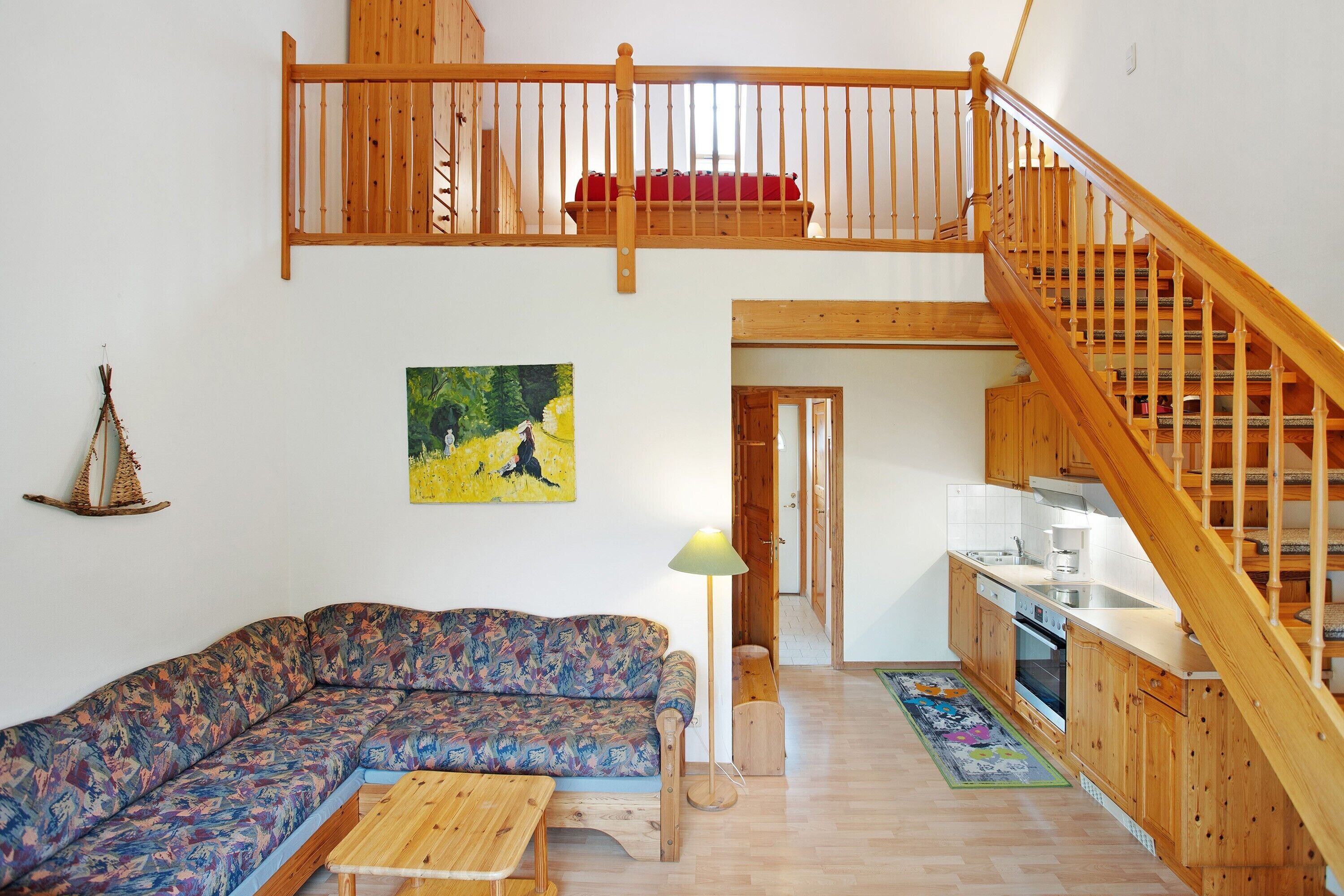 A loft-style living area with a wooden staircase, a sofa, a dining table, and a kitchen.