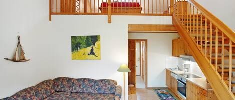 A loft-style living area with a wooden staircase, a sofa, a dining table, and a kitchen.