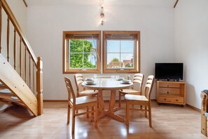 Un coin repas avec une table et des chaises en bois, un téléviseur et un escalier.