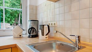Une cuisine moderne équipée d’un évier en acier inoxydable, d’une machine à café et d’une bouilloire posées sur le plan de travail.