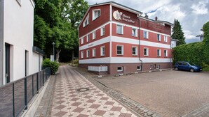 A multi-story building with a red and white facade, a tiled walkway, and a parked car. - Apartment "Haus Seeadler 9" with Shared Terrace & Wi-Fi (Koserow)