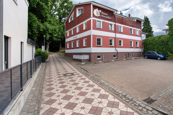 Een meerlaags gebouw met een rood-witte gevel, een betegeld voetpad en een geparkeerde auto.