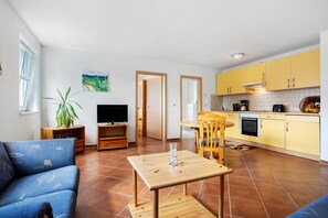 A living room with a sofa, TV, and dining area with yellow cabinets.