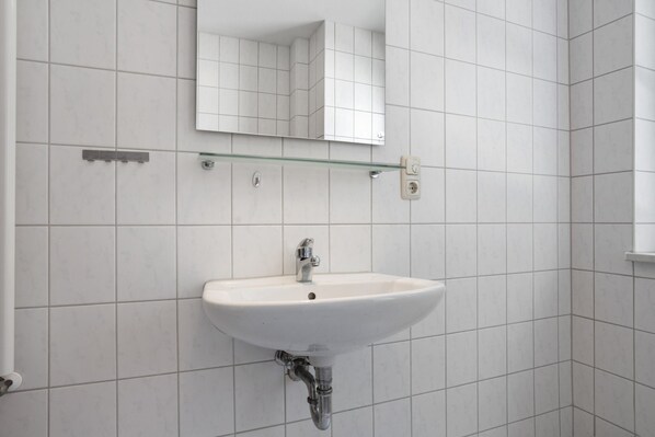 Une salle de bain avec un lavabo blanc, une étagère en verre au-dessus et un miroir.
