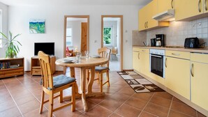 A kitchen with yellow cabinets, a dining table with chairs, a TV, and a bookshelf. - Apartment "Haus Seeadler 9" with Shared Terrace & Wi-Fi (Koserow)