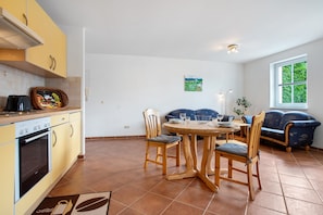A kitchen with yellow cabinets, a dining table with chairs, a blue sofa, and a window with a view of greenery.