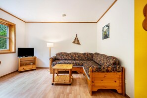 Una sala de estar con un sofá, un televisor sobre un mueble de madera, una mesita y una lámpara.
