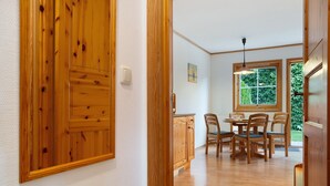 Una puerta de madera, un comedor con mesa y sillas, y una ventana con vistas a la vegetación.