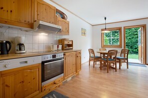 Una cocina con armarios de madera, un lavavajillas Siemens, una cafetera y un comedor con sillas y mesa de madera.