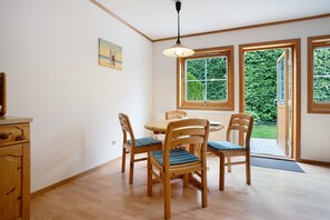 Un comedor con sillas de madera y una mesa, ventanas amplias con vistas a la vegetación, y una lámpara colgante.