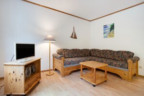 Una sala de estar con un mueble bajo de madera para el televisor, un sofá, una lámpara y un cuadro en la pared.