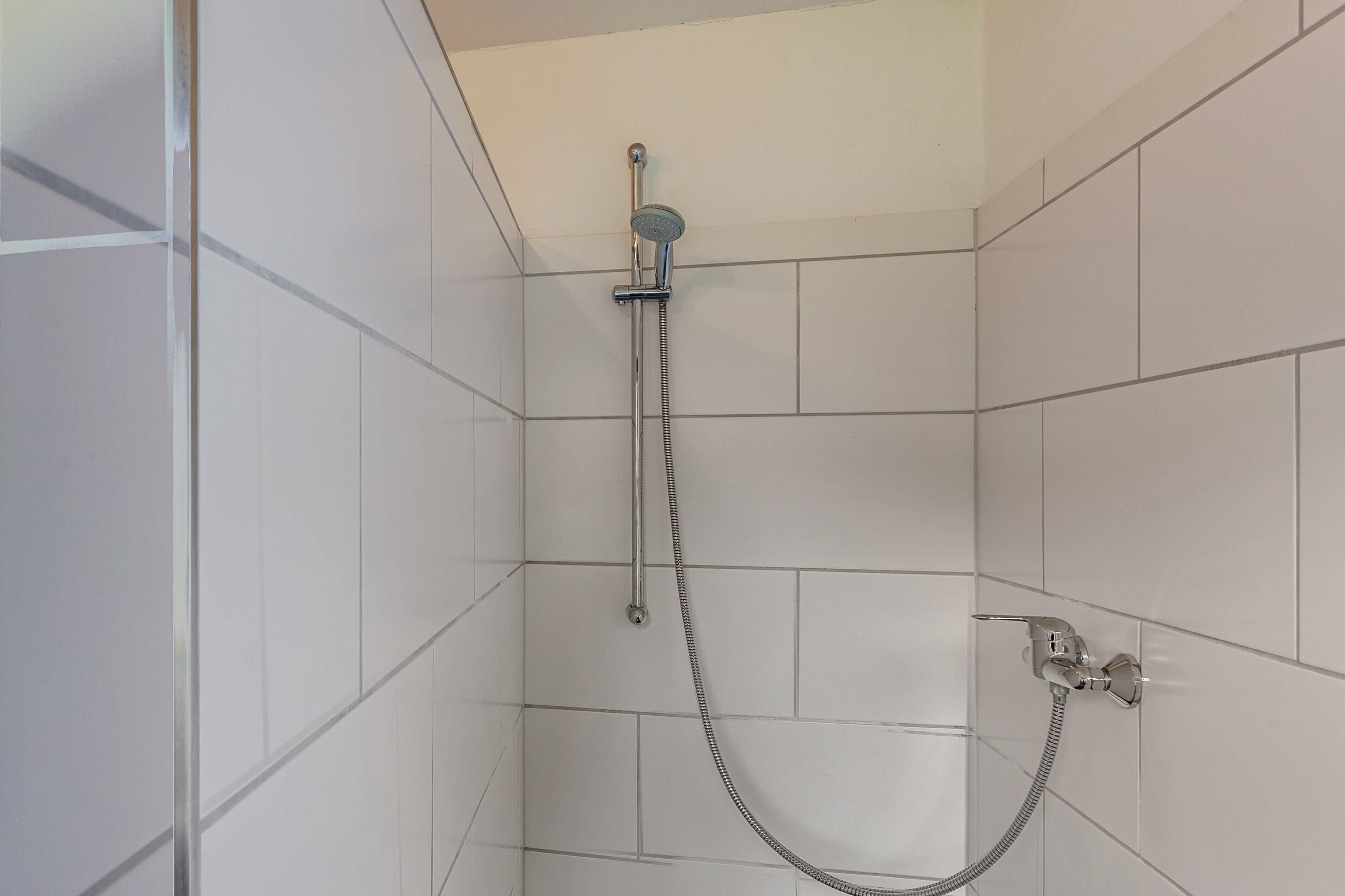A shower with a handheld showerhead and a flexible hose, tiled walls, and a corner shower enclosure.