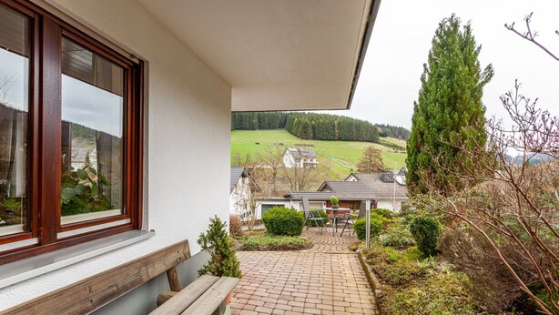 A building with a window, a wooden bench, a paved pathway, and a view of a green field and houses. - Apartment 'Ferienwohnung Rehsiepen' with Mountain View, Private Terrace and Wi-Fi (Schmallenberg)