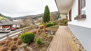 A residential building with a paved walkway, a wooden fence, and a view of a street with parked cars. - Apartment 'Ferienwohnung Rehsiepen' with Mountain View, Private Terrace and Wi-Fi (Schmallenberg)