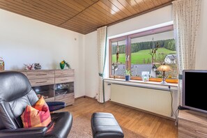 A living room with a leather sofa, a wooden cabinet, a window with a view of a green landscape, a radiator, and a television.