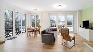 Un salón amplio con sofá, sillas, una mesa de comedor y grandes ventanas con vistas al exterior.